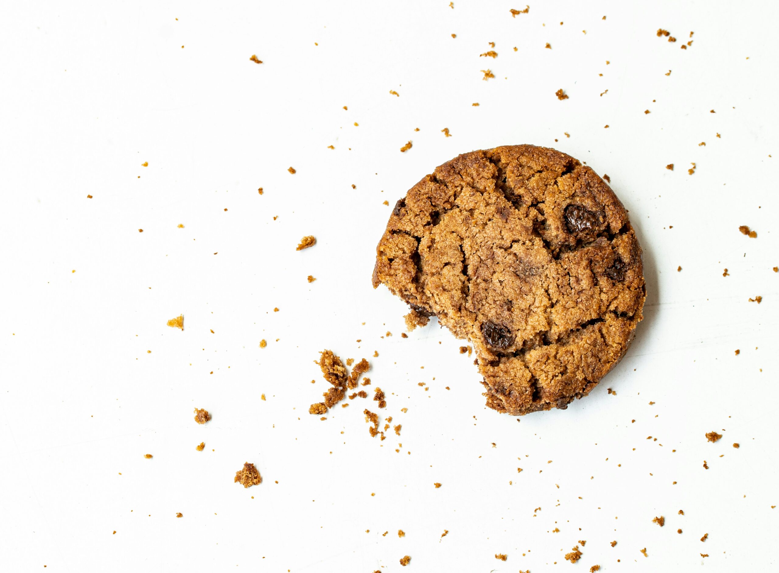 Ein angebissener Cookie liegt auf einer weißen Oberfläche mit zahlreichen Krümmeln rundherum.