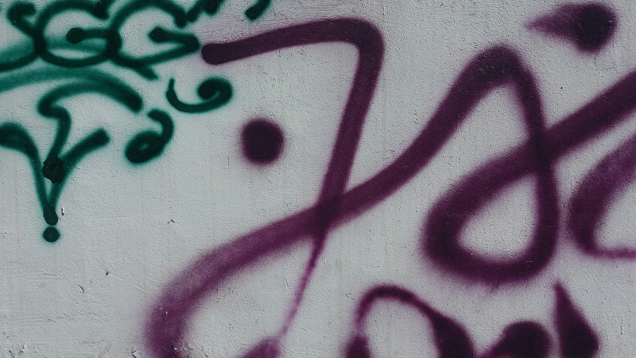 Auf einer grau-weißen Mauer sind verschiedene Graffiti-Tags zu sehen.