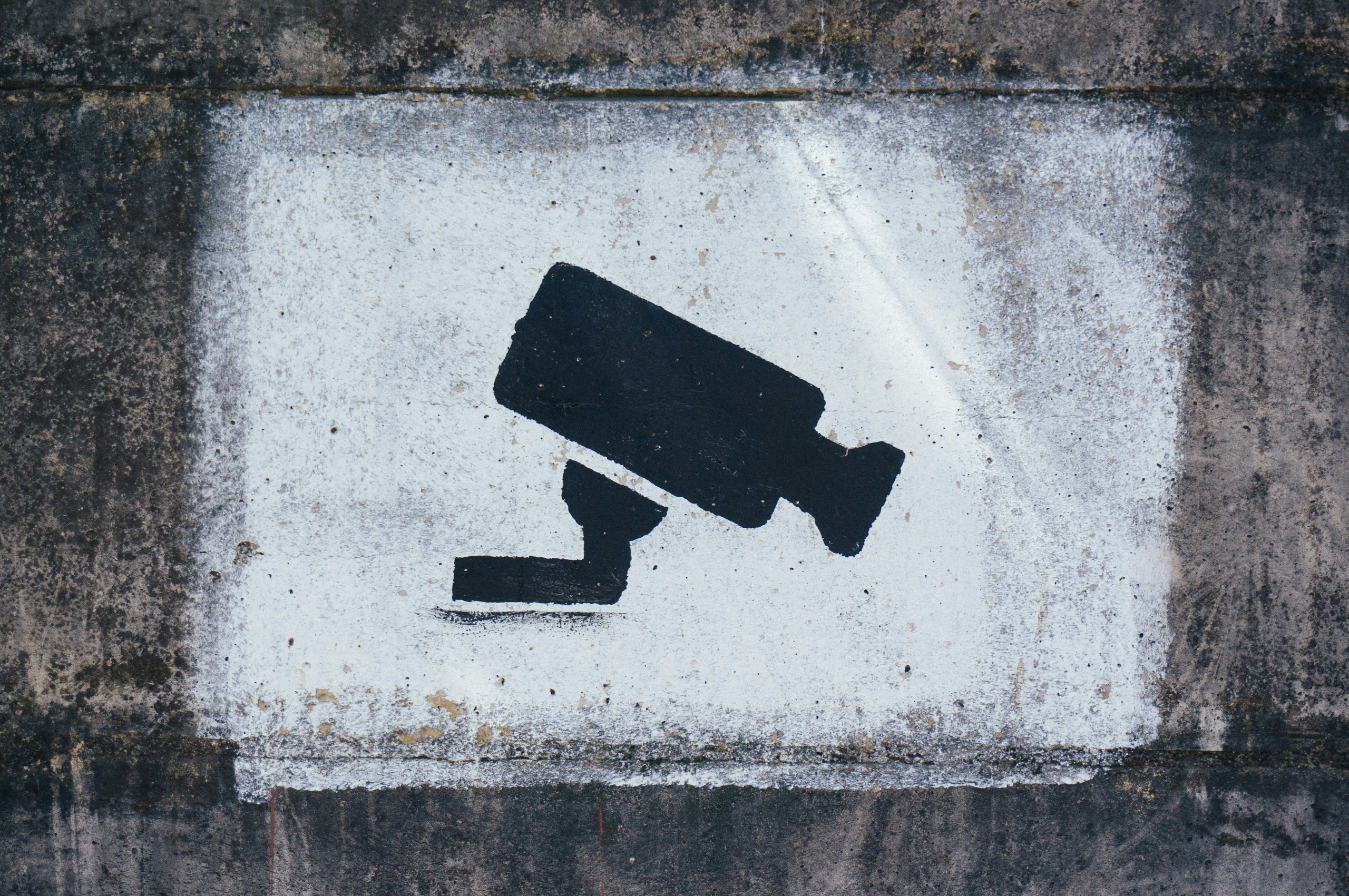 Eine stilisierte schwarze Kamera ist auf eine weiße Mauer gemalt.